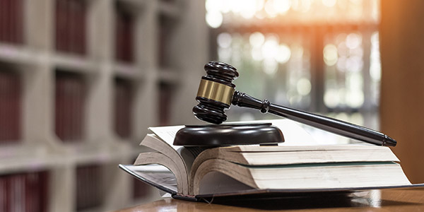 Image of a brown gavel sat on top of a stack of open books at a table in a library.
